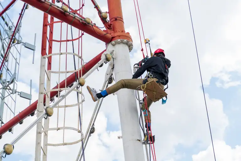 Worker with climbing equipment servicing a city TV tower at height